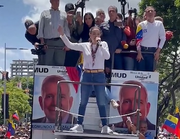 Una mujer habla por micrófono sobre una plataforma que tiene carteles con la foto de un candidato y banderas de Venezuela