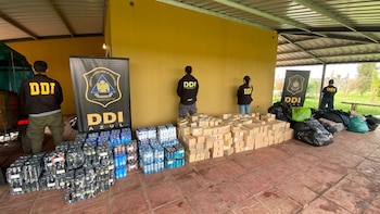 Cuatro agentes de la DDI de espaldas junto a grandes pilas de botellas de bebidas, cajas de cartón y bolsas de artículos incautados en el suelo
