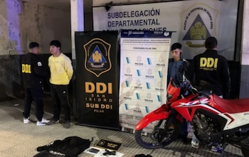 Dos jóvenes custodiados por efectivos de la DDI junto a una motocicleta roja y objetos incautados frente a carteles policiales