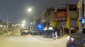 Varios efectivos policiales y personas reunidos de noche frente a la panadería Las Lomas junto a automóviles estacionados en una calle
