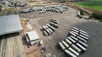 Vista aérea de un amplio estacionamiento con hileras de camiones de carga junto a carriles de acceso y edificios de control