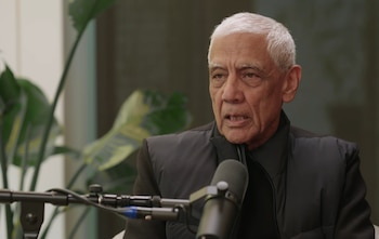 Primer plano de Vinod Khosla, un hombre de edad avanzada con cabello blanco y chaleco oscuro, hablando frente a un micrófono. Plantas verdes borrosas al fondo