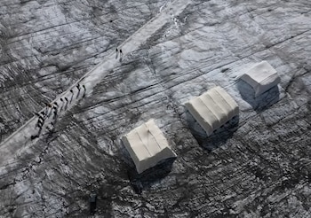 Vista aérea de un glaciar con tres cubiertas blancas rectangulares y varias personas sobre un camino trazado en el hielo