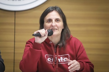 Una mujer con sudadera roja sostiene un micrófono negro frente a un panel de madera