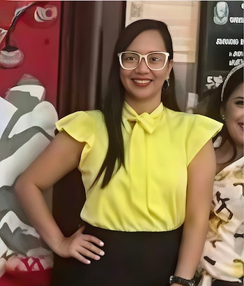 Retrato de Alejandra Verónica Romero Castillo, mujer de cabello oscuro y gafas blancas, sonriendo a cámara, vistiendo blusa amarilla y falda negra, con una mano en la cadera