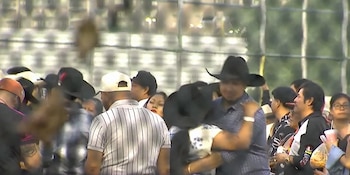 Multitud de personas en un evento al aire libre; algunas llevan sombreros y gorras. Fondo borroso con estructura de malla o valla