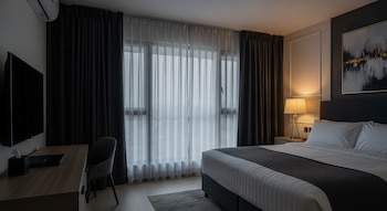 Vista general de una habitación en penumbra con cortinas blackout cerradas. Se observa una cama ordenada, un televisor en la pared y una lámpara de noche encendida.