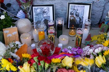 Ramos de flores de varios colores, velas encendidas y dos fotografías enmarcadas colocadas junto a un muro