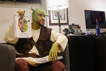 Bad Bunny, vestido como Shrek con la cara y las manos verdes, sostiene un guion blanco con su foto mitad Bad Bunny, mitad Shrek