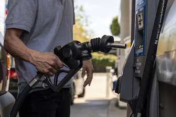 Una persona sostiene una boquilla negra de combustible conectada a un surtidor junto a un automóvil