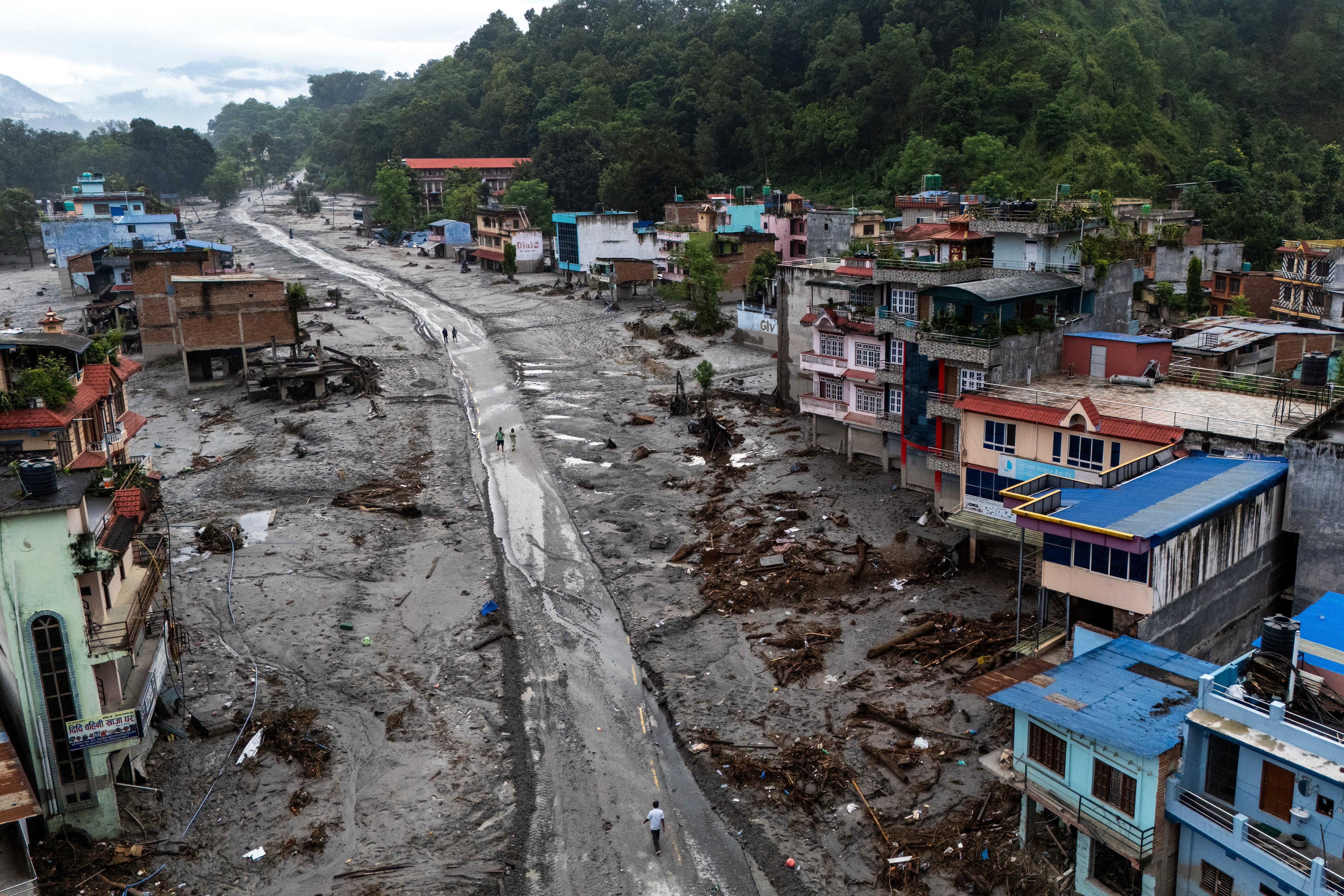 Una vista aérea tomada por un dron muestra a personas caminando por una carretera y casas cubiertas de lodo tras mortales inundaciones repentinas y deslizamientos de tierra, en Devighat, distrito de Nuwakot, Nepal (REUTERS/Athit Perawongmetha)