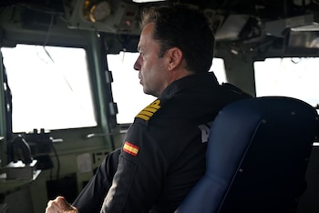 Hombre con uniforme militar oscuro e insignia española en la manga, sentado de perfil en una cabina frente a una ventana