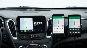 Pantalla del tablero de un automóvil y dos teléfonos inteligentes en soportes con una aplicación de mapas en pantalla.