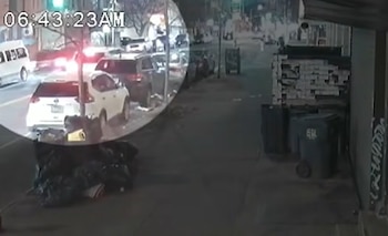 Captura de cámara de seguridad con una marca de tiempo que muestra una calle con automóviles estacionados, bolsas de basura y contenedores
