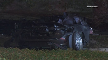 Los restos destruidos de un automóvil deportivo de color oscuro se encuentran junto a la vegetación durante la noche