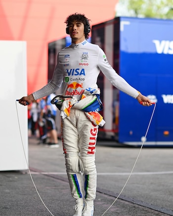 Un piloto con vestimenta blanca de carreras y auriculares sostiene una cuerda de saltar frente a un camión de equipo