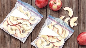 Una ilustración en acuarela con manzanas enteras y troceadas en bolsas de plástico con cierre sobre un fondo de tablas de madera.