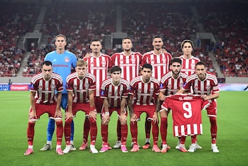 Once jugadores de fútbol posan en dos filas sobre el césped, diez con uniforme a rayas rojas y blancas y uno con camiseta azul