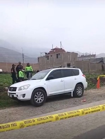 Vehículo SUV blanco en el margen de una vía de tierra. Personas con uniforme están junto al coche. Una cinta amarilla con 'ZONA RESTRINGIDA' visible