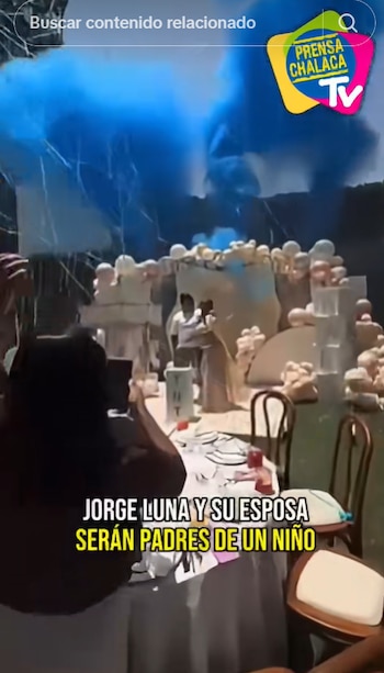 Una pareja permanece junto a globos y humo azul en una celebración con mesas decoradas y un texto explicativo en pantalla