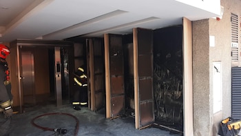 Dos bomberos trabajan en el interior de un edificio con severos daños por incendio, que incluye paredes ennegrecidas, paneles quemados y una manguera