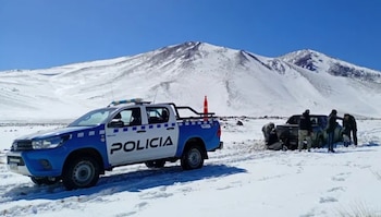 Camioneta azul y blanca de la policía en un terreno cubierto de nieve frente a varias personas junto a una montaña