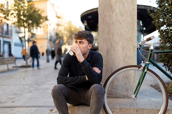 Un joven sentado mientras toma un café, junto a una bicicleta.