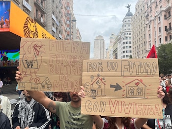 Varias personas sostienen dos carteles de cartón con consignas escritas a mano sobre la vivienda en una calle con edificios de fondo