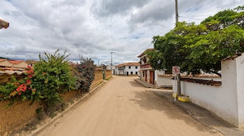Carretera asfaltada y mojada con señalización vial, rodeada de laderas verdes, árboles y una casa en una zona rural montañosa
