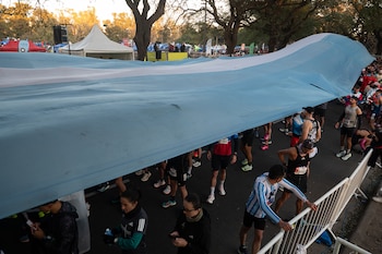 Varios corredores con números de competencia permanecen bajo una gran bandera de Argentina extendida a lo largo de la calle