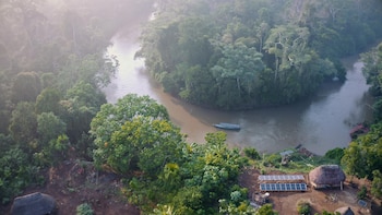 Vista aérea de un río en la selva, una embarcación con paneles en el techo y filas de paneles solares junto a chozas tradicionales