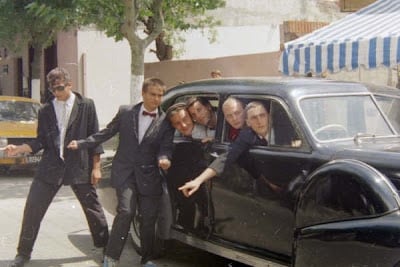 Los Fabulosos Cadillacs posan con trajes formales junto a un automóvil negro durante su estadía en Mar del Plata.