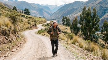 Un hombre con chullo y mochila camina por un camino de tierra sin asfaltar en un entorno montañoso.