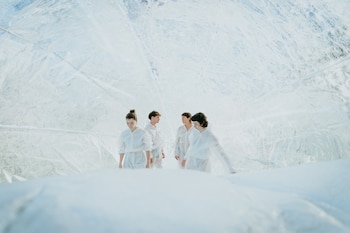 Cuatro personas vestidas de blanco dentro de una estructura abovedada y translúcida de material arrugado, con luz brillante