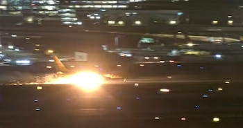 Vista nocturna de un avión en una pista de aterrizaje con un resplandor de fuego y chispas debajo del fuselaje