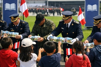 Cuatro niños reciben publicaciones de adultos uniformados en un campo verde. Se observan banderas de Perú y banners azules con un logo de libro abierto.