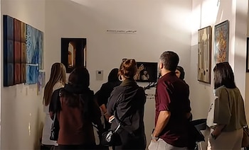 Personas de espaldas contemplan diversas pinturas colgadas en las paredes blancas de una sala de exhibición