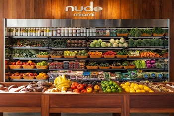 Un estante de supermercado Nude Miami lleno de frutas frescas como plátanos, limas, limones y tomates, además de verduras, salsas y productos envasados