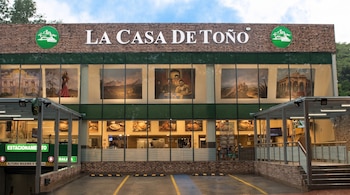 Fachada de ladrillo y ventanales grandes del restaurante La Casa de Toño, con estacionamiento subterráneo, señales de tráfico y un árbol al fondo.