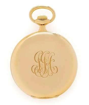 Un reloj de bolsillo redondo de oro pulido sobre un fondo blanco. La tapa trasera presenta las iniciales "JJA" grabadas en estilo caligráfico ornamental