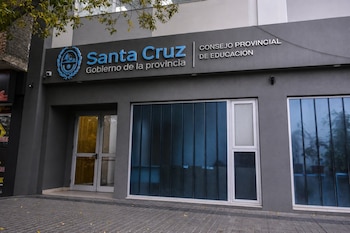 Fachada de edificio gris con cartel de Santa Cruz Gobierno de la provincia y Consejo Provincial de Educación. Incluye puerta de vidrio y ventanas