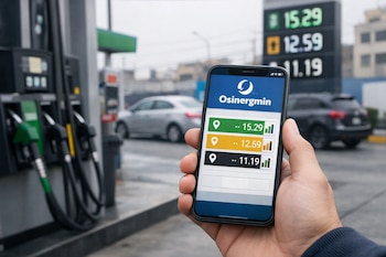 Una mano sostiene un teléfono inteligente con la aplicación Osinergmin mostrando precios de combustibles, con surtidores y un cartel de precios al fondo.