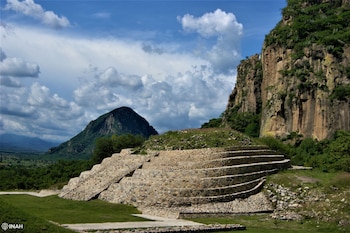 Estructura piramidal con terrazas de piedra y escalinatas al pie de una montaña rocosa bajo un cielo nublado