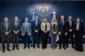 Nueve personas vistiendo trajes formales posan frente a una pared azul con el escudo del Ministerio de Seguridad Nacional de Argentina