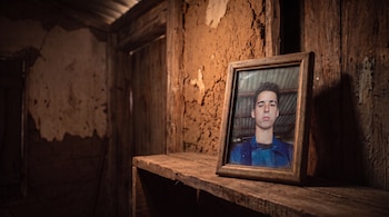 Marco de madera con la fotografía de un joven sobre un estante de madera ante una pared de barro y tablas.
