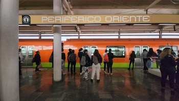 Pasajeros permanecen en el andén de la estación Periférico Oriente junto a un tren naranja del sistema de transporte