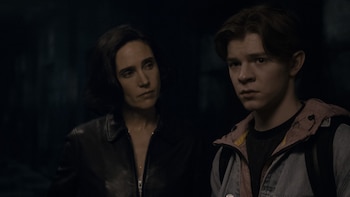Jennifer Connelly viste una chaqueta de cuero negra y Oakes Fegley lleva una chaqueta sobre un buzo con capucha en un entorno oscuro