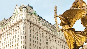 Fachada de un edificio clásico de varios pisos con tejado verde y una estatua dorada de un ángel en primer plano a la derecha