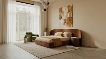 Dormitorio luminoso con cama tapizada en terracota, sábanas claras, sillón verde, mesitas de mármol, alfombra beige, ventanal y cuadro abstracto.