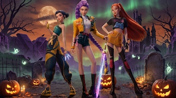 Tres mujeres animadas de pie en un cementerio con luna llena, lápidas, espectros flotantes y calabazas talladas iluminadas.